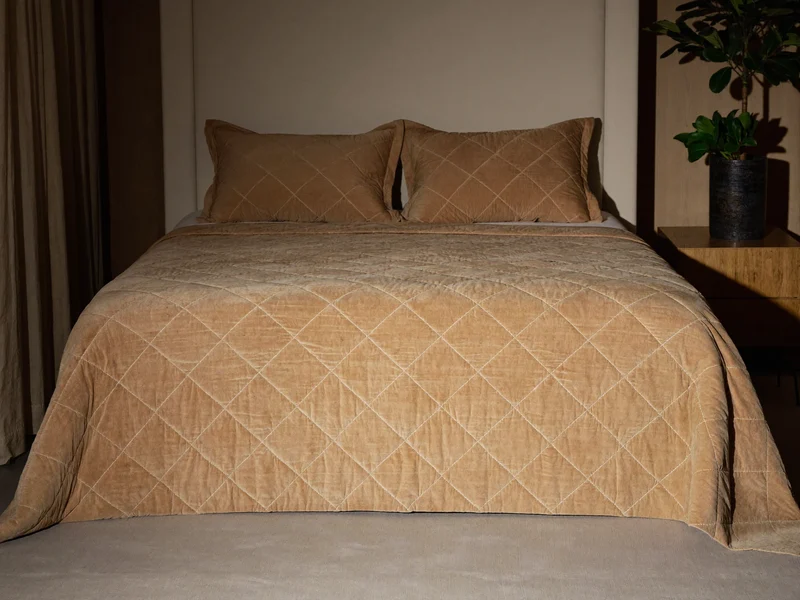 Couvre-lit matelassé sable et deux housses de coussin au pied du lit